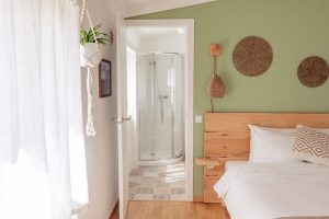 Bright and cozy ensuite double room at Moka Surf House in Ericeira featuring a private bathroom, wooden decor, and natural light, ideal for a surf and yoga retreat.