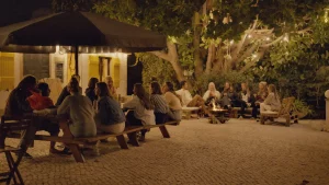 Guests relaxing in the garden of Moka Surf House during an evening gathering with firepit and warm lights under the trees.