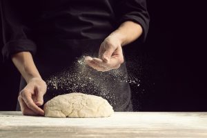 Close-up of a chef preparing handmade dough on a floured table, symbolizing the focus on homemade vegetarian and vegan Italian cuisine at Moka Surf House.