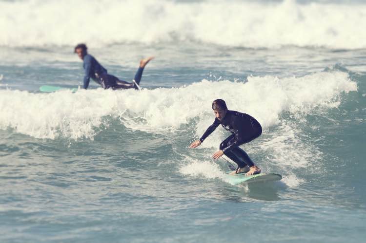 intermediate-surf-session-ericeira-green-wave-moka-surf-house Intermediate surfer riding a green wave during a surf session in Ericeira, with another surfer in the background, part of the Surf experience at Moka Surf House.