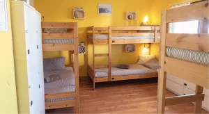 Spacious shared room at Moka Surf & Yoga House in Portugal with wooden bunk beds, yellow walls, individual reading lights, and lockers.