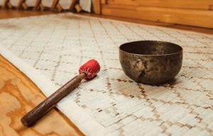 Close-up of meditation beads and a singing bowl on a wooden table with natural light reflections.