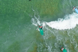 Aerial view of a surf student riding a wave on a green board during a lesson in Ericeira, part of the Moka Surf House Surf School Package.