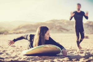 Woman practicing paddling technique on the sand with surfboard and instructor at Moka Surf House in Ericeira.