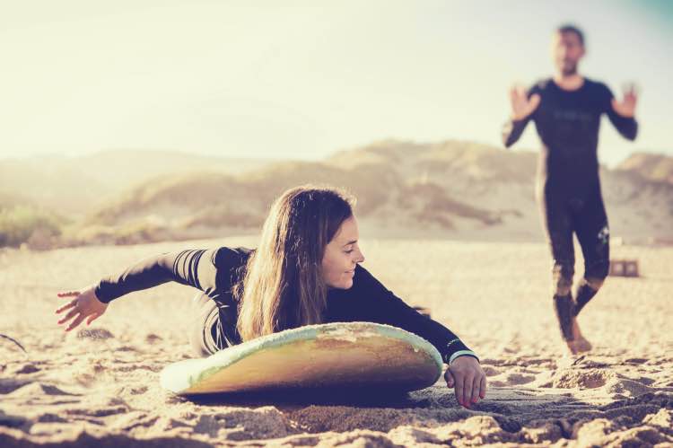 surf-lesson-paddling-technique-ericeira-beach-moka-surf-house Woman practicing paddling technique on the sand with surfboard and instructor at Moka Surf House in Ericeira.
