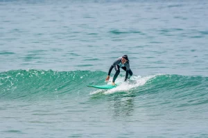 Woman riding a small green wave during a surf session in Ericeira, part of the Yoga & Surf Package by Moka Surf House.