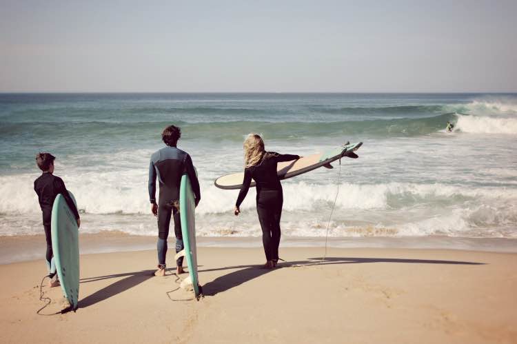 surfers-ready-to-enter-water-ericeira-private-lesson-moka-surf-house Three surfers standing on the shore, ready to enter the ocean with boards in hand during a private surf lesson in Ericeira.