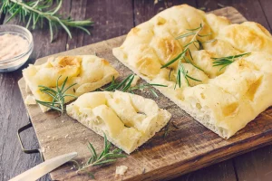Freshly baked Italian focaccia with rosemary on a wooden board, served at the guesthouse in Ericeira, Portugal.