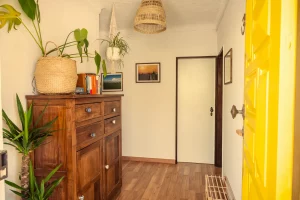 Bright and welcoming entrance of Moka Surf House & Yoga Retreat in Ericeira with yellow door, wooden cabinet, books, and indoor plants.