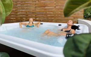 Two women relaxing in an outdoor jacuzzi surrounded by plants and a wooden privacy fence at Moka guesthouse in Ericeira.