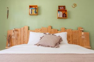 Private single room with natural wooden headboard, cushion, green wall, and soft lighting at a yoga retreat in Ericeira.