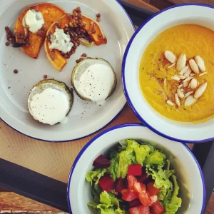 Vegetarian meal with roasted pumpkin and lentils, baked zucchini with cheese, carrot soup topped with almonds, and a fresh green salad with beets and tomatoes.
