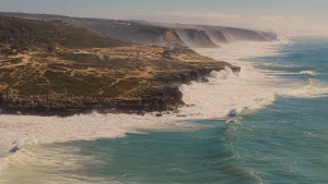 erial view of the dramatic Atlantic coastline near Ericeira, Portugal, with cliffs and powerful ocean waves crashing against the shore.