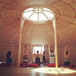 Group yoga session in a sunlit yurt at Moka Surf House, with participants seated and arms raised.