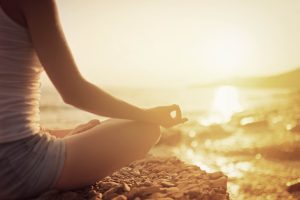 Person meditating in lotus pose at sunrise on a rocky beach in Ericeira during a yoga workshop.