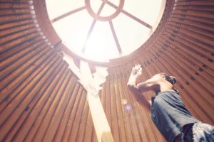 Woman practicing yoga inside the yurt with arms raised, bathed in natural light, part of the Moka Surf House experience.
