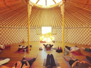 Group of people practicing yoga inside a traditional wooden yurt during a Yoga & Surf retreat in Ericeira, Portugal.